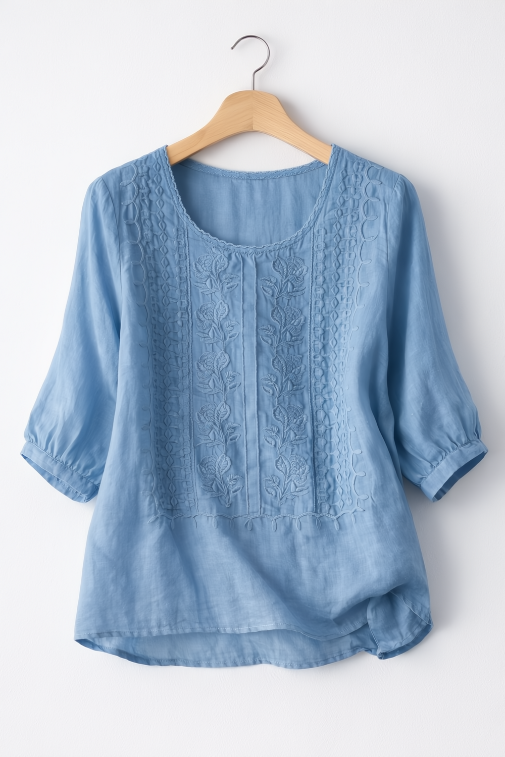 Blue embroidered blouse on a hanger against a white background