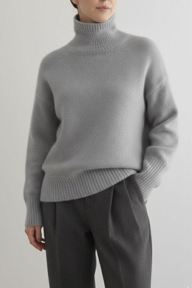 Person wearing a gray turtleneck sweater and dark pants on a light gray background