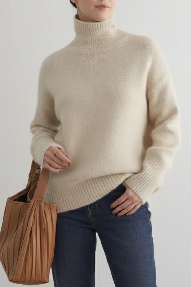 Person wearing a beige sweater and blue jeans holding a brown bag on a light gray background