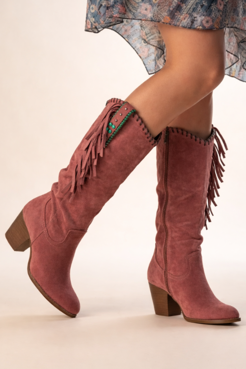 Pink suede boots with fringe on a plain background